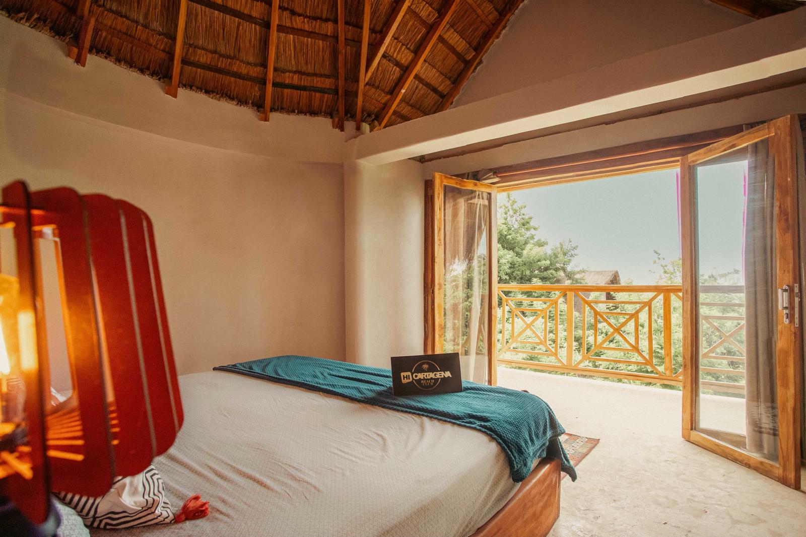 Bedroom beneath a thatched roof opening onto a wooden balcony
