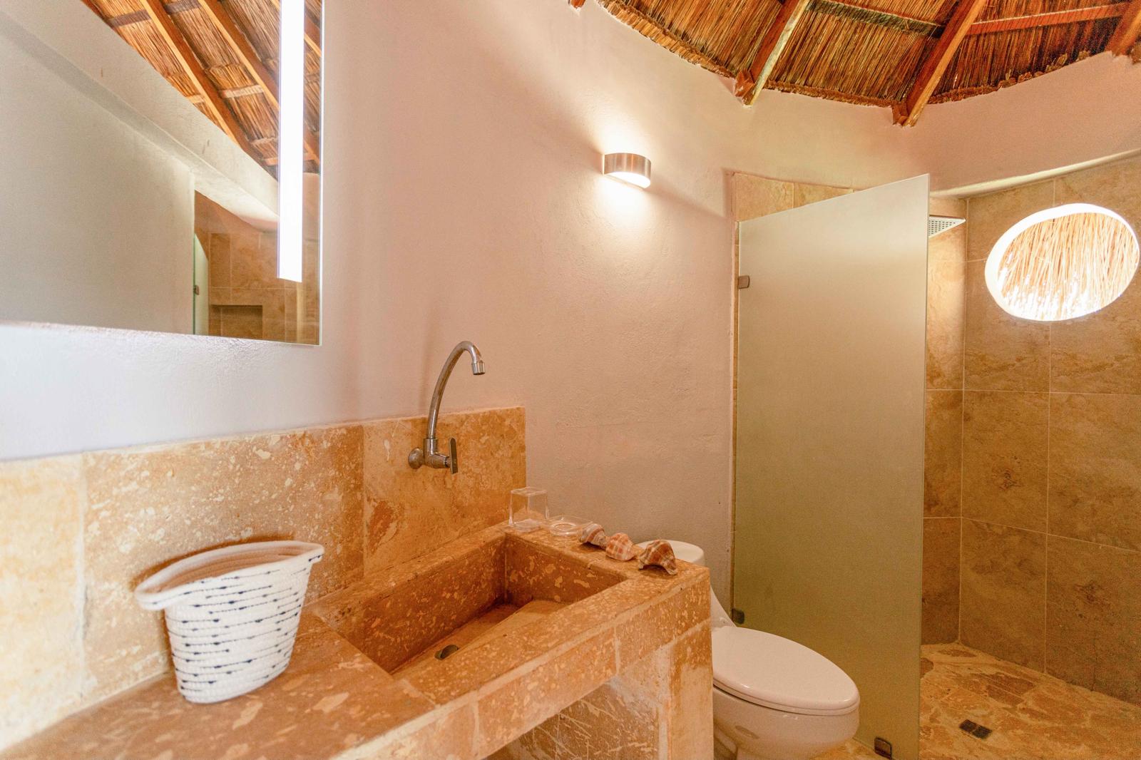 Bathroom carved in coral stone beneath a thatched ceiling